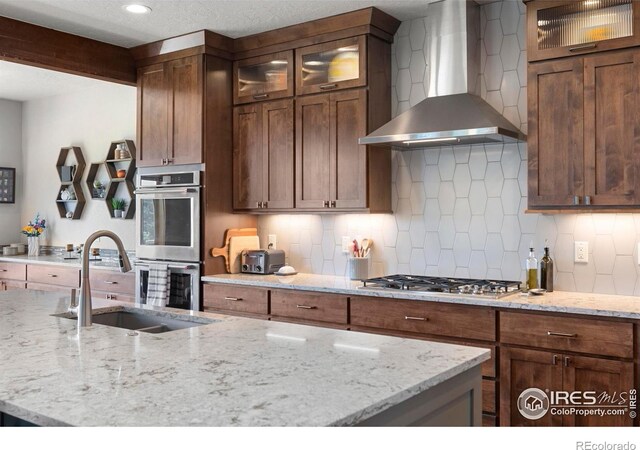 37044 Soaring Eagle Cir, Severance, CO 80550 - kitchen featuring wall chimney exhaust hood, stainless steel appliances, backsplash, and light stone counters