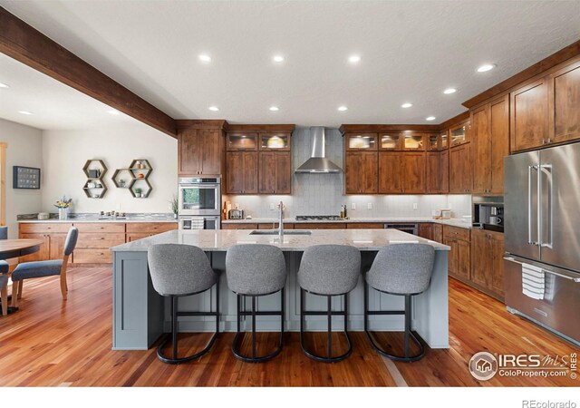 37044 Soaring Eagle Cir, Severance, CO 80550 - kitchen with appliances with stainless steel finishes, wall chimney range hood, a kitchen island with sink, light wood-style floors, and recessed lighting