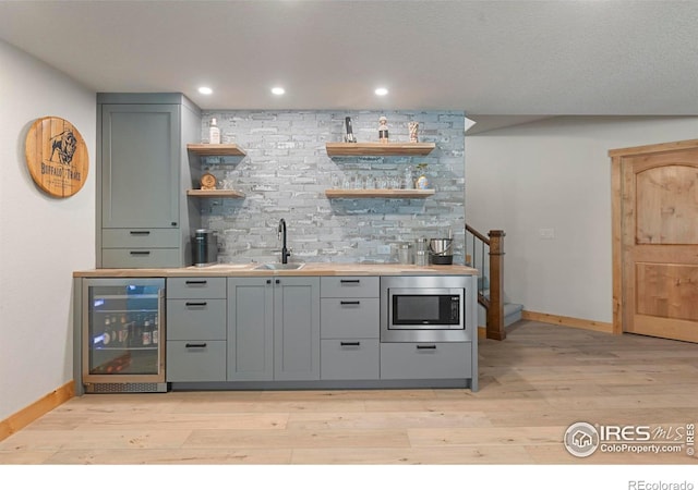 37044 Soaring Eagle Cir, Severance, CO 80550 - indoor wet bar featuring wine cooler, stainless steel microwave, light wood finished floors, tasteful backsplash, and recessed lighting