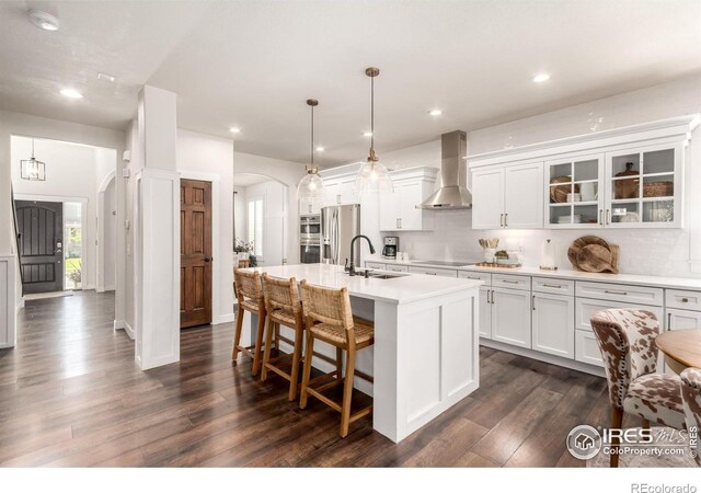 3290 Discovery Ct, Broomfield, CO 80023 - kitchen featuring wall chimney range hood, arched walkways, dark wood-type flooring, an island with sink, and recessed lighting