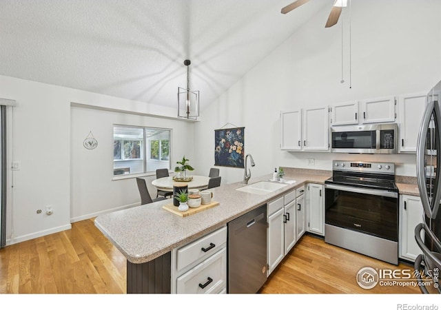951 Vetch Cir, Lafayette, CO 80026 - kitchen featuring appliances with stainless steel finishes, a peninsula, light wood finished floors, vaulted ceiling, and white cabinets