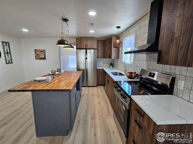202 N 7th Ave, Sterling, CO 80751 - kitchen featuring stainless steel appliances, wall chimney range hood, wooden counters, light wood-type flooring, and recessed lighting
