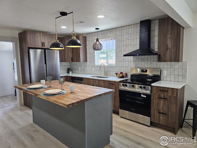 202 N 7th Ave, Sterling, CO 80751 - kitchen featuring appliances with stainless steel finishes, wall chimney exhaust hood, light wood finished floors, tasteful backsplash, and a textured ceiling