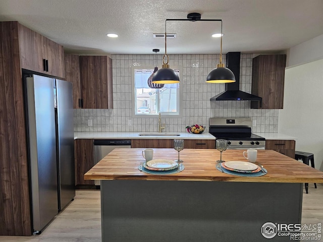 202 N 7th Ave, Sterling, CO 80751 - kitchen with appliances with stainless steel finishes, range hood, backsplash, light wood finished floors, and a textured ceiling