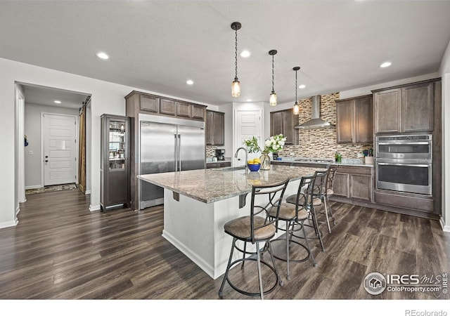 12648 Canoe St, Firestone, CO 80504 - kitchen featuring stainless steel appliances, wall chimney exhaust hood, recessed lighting, dark brown cabinets, and a breakfast bar area