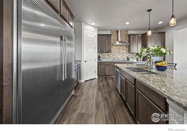 12648 Canoe St, Firestone, CO 80504 - kitchen with appliances with stainless steel finishes, wall chimney exhaust hood, dark wood-style floors, dark brown cabinets, and light stone countertops