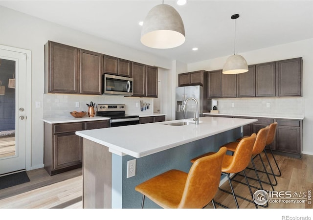 5199 Beckworth St, Timnath, CO 80547 - kitchen featuring appliances with stainless steel finishes, decorative backsplash, light wood finished floors, dark brown cabinets, and a kitchen breakfast bar