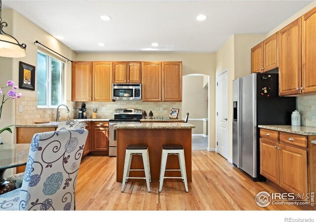8119 Lighthouse Ln, Windsor, CO 80528 - kitchen with appliances with stainless steel finishes, light wood-style flooring, a center island, arched walkways, and decorative backsplash