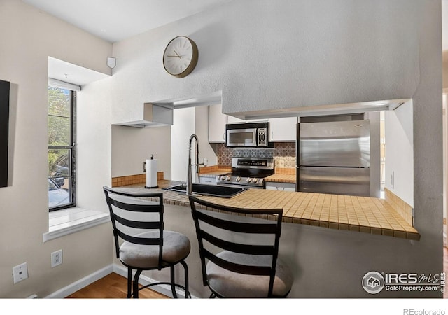 2279 Spruce St Unit 8, Boulder, CO 80302 - kitchen featuring stainless steel appliances, a peninsula, tasteful backsplash, white cabinets, and a kitchen bar
