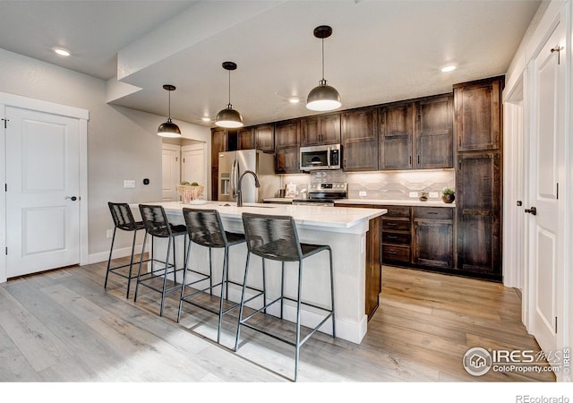 265 High Point Dr Unit 202, Longmont, CO 80504 - kitchen with stainless steel appliances, an island with sink, dark brown cabinets, decorative backsplash, and light countertops