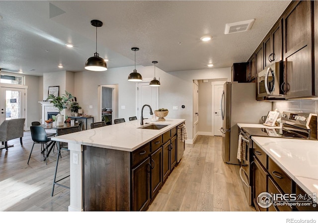 265 High Point Dr Unit 202, Longmont, CO 80504 - kitchen with stainless steel appliances, a kitchen island with sink, light wood-style floors, a kitchen bar, and dark brown cabinets