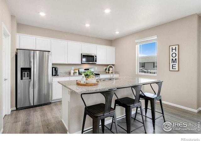 6818 Whisper Trail Ln, Wellington, CO 80549 - kitchen featuring appliances with stainless steel finishes, light wood finished floors, a kitchen island with sink, white cabinetry, and a breakfast bar