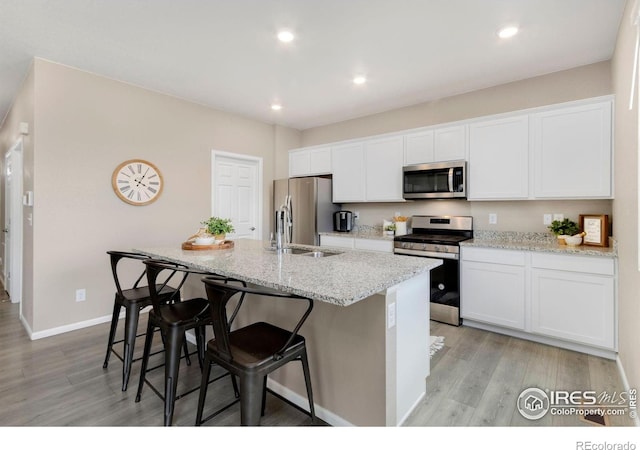 6818 Whisper Trail Ln, Wellington, CO 80549 - kitchen with stainless steel appliances, a center island with sink, light wood-style floors, white cabinets, and recessed lighting