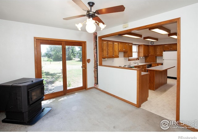 19089 Chambers Dr, Sterling, CO 80751 - kitchen featuring freestanding refrigerator, a wood stove, light colored carpet, brown cabinetry, and a peninsula