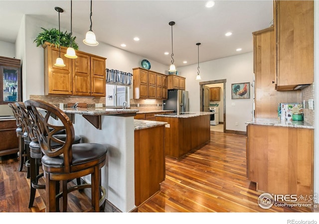 973 Skipping Stone Ct, Timnath, CO 80547 - kitchen featuring freestanding refrigerator, a center island, brown cabinets, wood-type flooring, and tasteful backsplash