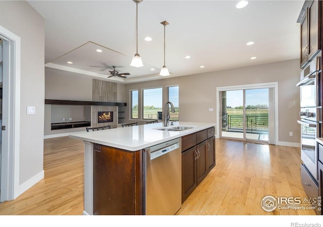 6928 Summerwind Ct, Timnath, CO 80547 - kitchen featuring stainless steel dishwasher, a fireplace, light wood-style floors, an island with sink, and healthy amount of natural light