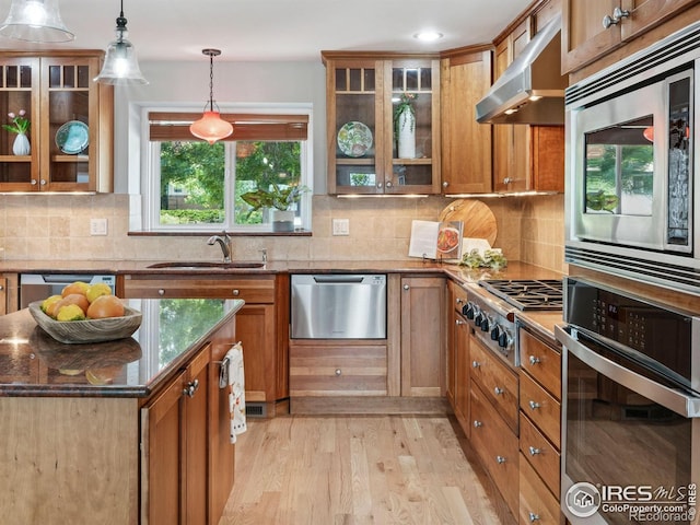 2695 Stanford Ave, Boulder, CO 80305 - kitchen with appliances with stainless steel finishes, wall chimney exhaust hood, brown cabinetry, dark stone countertops, and light wood-style flooring