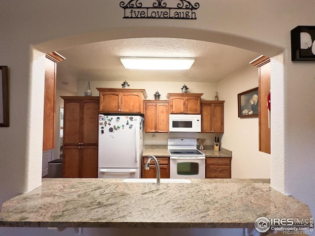 4101 Crittenton Ln Unit 102, Wellington, CO 80549 - kitchen with white appliances, arched walkways, a peninsula, and light stone counters
