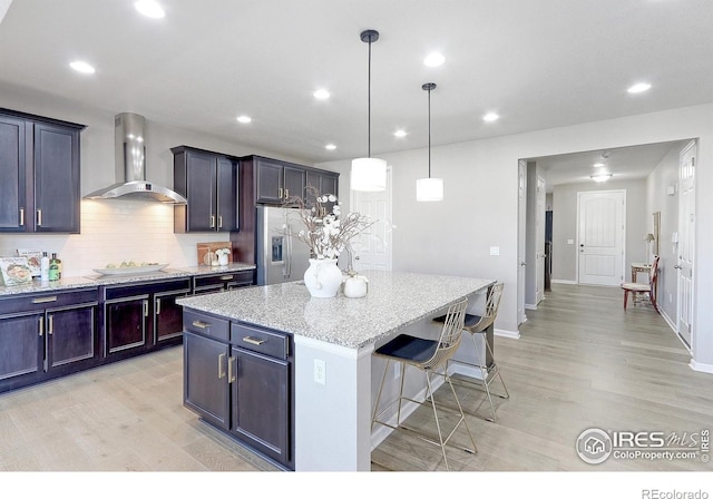16021 Williams Pl, Broomfield, CO 80023 - kitchen with stainless steel fridge with ice dispenser, wall chimney exhaust hood, light wood-type flooring, a kitchen bar, and recessed lighting
