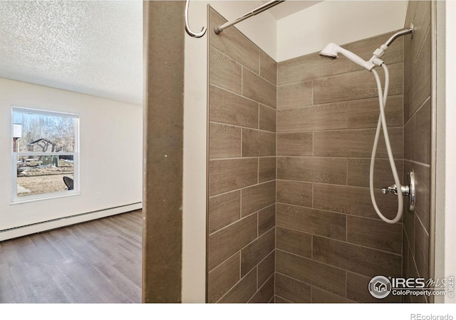 1620-1626 E 17th St, Loveland, CO 80538 - bathroom with tiled shower, wood finished floors, a baseboard radiator, and a textured ceiling