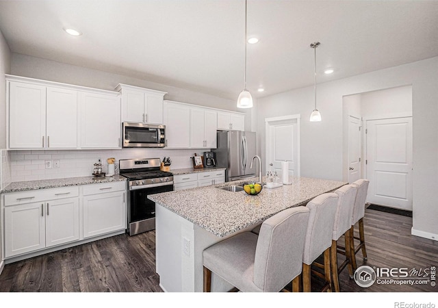 7415 E 158th Pl, Thornton, CO 80602 - kitchen featuring stainless steel appliances, dark wood finished floors, backsplash, a center island with sink, and white cabinetry