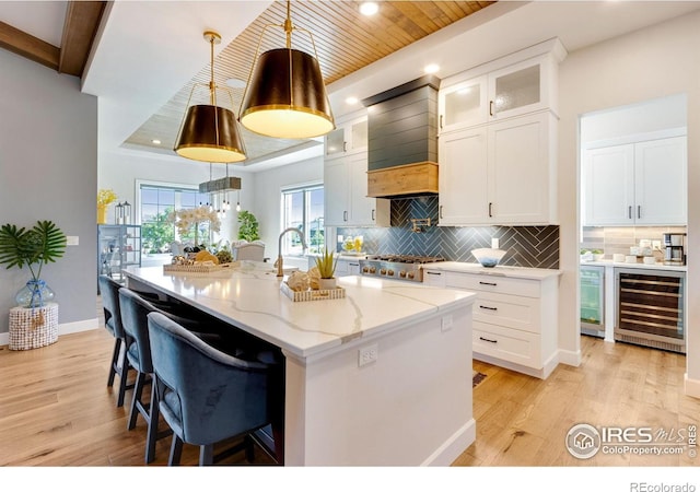 4198 Prestwich Ct, Timnath, CO 80547 - kitchen with wine cooler, light wood finished floors, white cabinetry, a kitchen island with sink, and recessed lighting