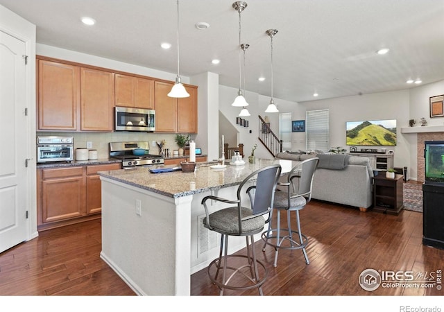 833 Carbonate Ln, Erie, CO 80516 - kitchen with appliances with stainless steel finishes, dark wood-style floors, recessed lighting, light stone countertops, and a center island with sink