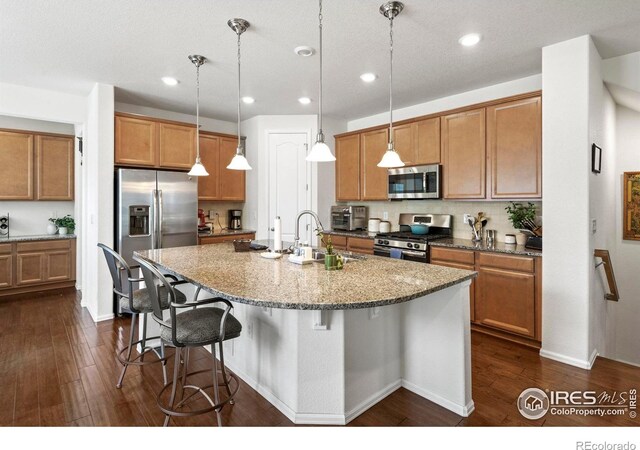 833 Carbonate Ln, Erie, CO 80516 - kitchen featuring stainless steel appliances, brown cabinets, a kitchen breakfast bar, dark wood-style flooring, and recessed lighting
