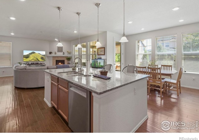 833 Carbonate Ln, Erie, CO 80516 - kitchen with stainless steel dishwasher, dark wood-type flooring, a lit fireplace, a center island with sink, and light stone counters