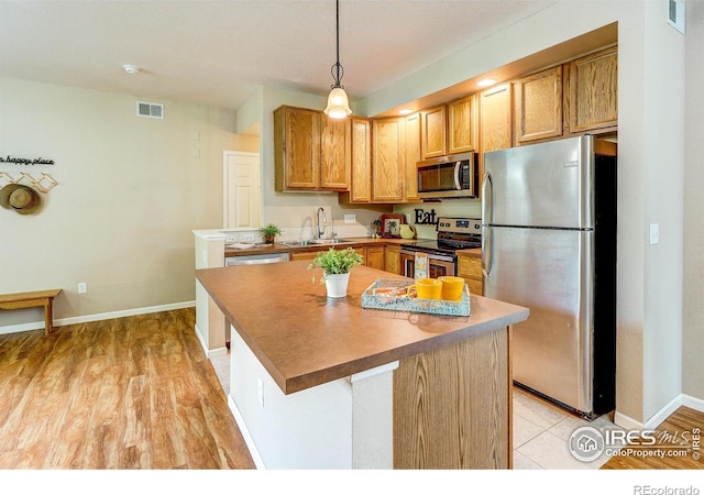 2131 Grays Peak Dr Unit 102, Loveland, CO 80538 - kitchen with appliances with stainless steel finishes, decorative light fixtures, a kitchen island, and light wood-type flooring