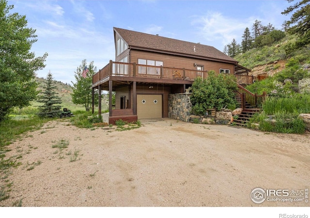 228 Mount Everest Dr, Livermore, CO 80536 - view of front facade with a garage, a wooden deck, driveway, stone siding, and stairway