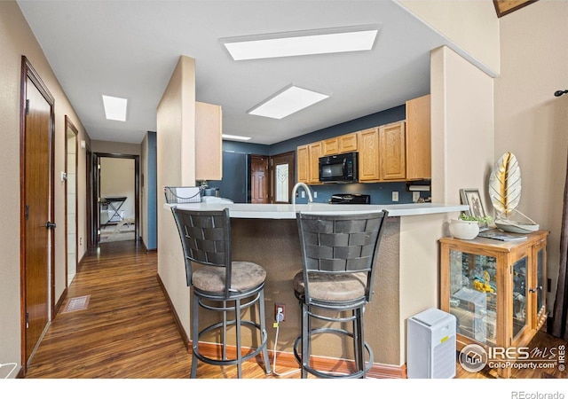 228 Mount Everest Dr, Livermore, CO 80536 - kitchen with black microwave, dark wood finished floors, a skylight, a kitchen breakfast bar, and a peninsula