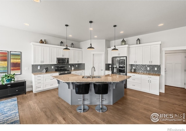 401 Cascade Ct, Johnstown, CO 80534 - kitchen featuring stainless steel appliances, decorative backsplash, a kitchen breakfast bar, a kitchen island with sink, and white cabinetry