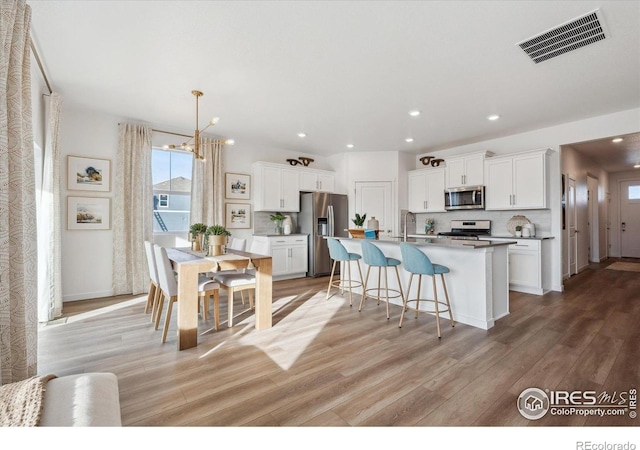 2239 Base St, Fort Lupton, CO 80621 - kitchen featuring appliances with stainless steel finishes, light wood-style flooring, white cabinets, a breakfast bar, and recessed lighting