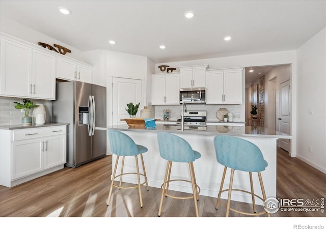 2239 Base St, Fort Lupton, CO 80621 - kitchen featuring stainless steel appliances, backsplash, a breakfast bar, light wood-style flooring, and recessed lighting