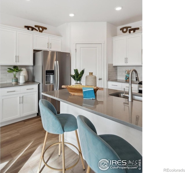 2239 Base St, Fort Lupton, CO 80621 - kitchen featuring stainless steel refrigerator with ice dispenser, a breakfast bar, decorative backsplash, white cabinets, and recessed lighting
