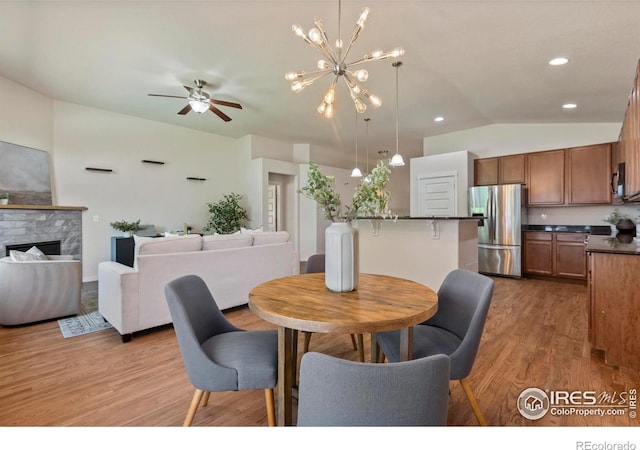 2968 Hydra Dr, Loveland, CO 80537 - dining space featuring vaulted ceiling, light wood finished floors, a ceiling fan, a fireplace, and a chandelier