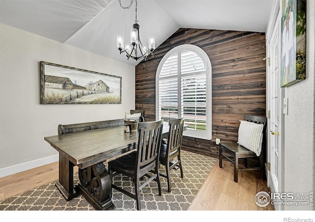 1115 Kestrel Rd, Eaton, CO 80615 - dining space featuring wood walls, a chandelier, vaulted ceiling, wood finished floors, and an accent wall