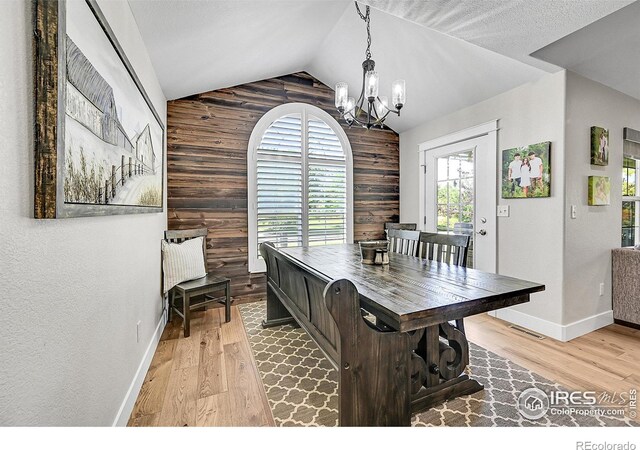 1115 Kestrel Rd, Eaton, CO 80615 - dining area with wooden walls, a chandelier, lofted ceiling, light wood-style floors, and an accent wall