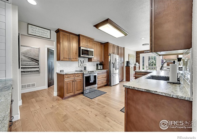 1115 Kestrel Rd, Eaton, CO 80615 - kitchen featuring stainless steel appliances, light wood finished floors, backsplash, brown cabinetry, and recessed lighting