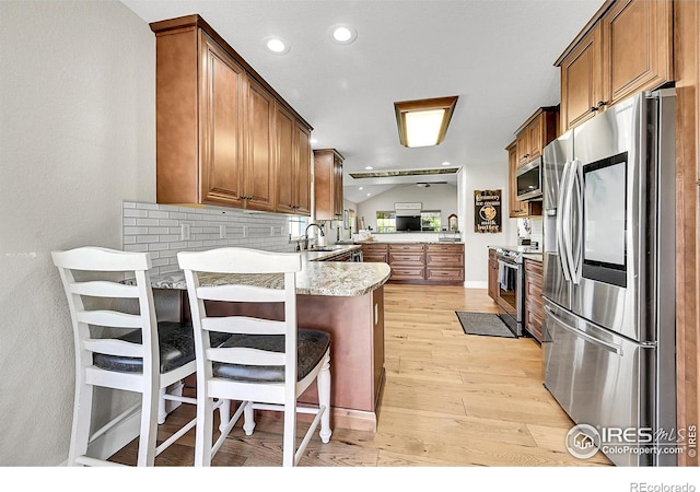 1115 Kestrel Rd, Eaton, CO 80615 - kitchen with stainless steel appliances, a peninsula, light wood finished floors, brown cabinetry, and recessed lighting
