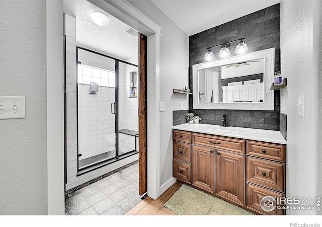 1115 Kestrel Rd, Eaton, CO 80615 - bathroom featuring vanity, a shower stall, decorative backsplash, wood finished floors, and a textured wall