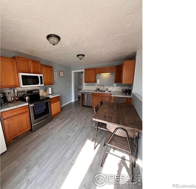 1031 N Lincoln Ave, Loveland, CO 80537 - kitchen with appliances with stainless steel finishes, brown cabinets, light countertops, light wood finished floors, and backsplash