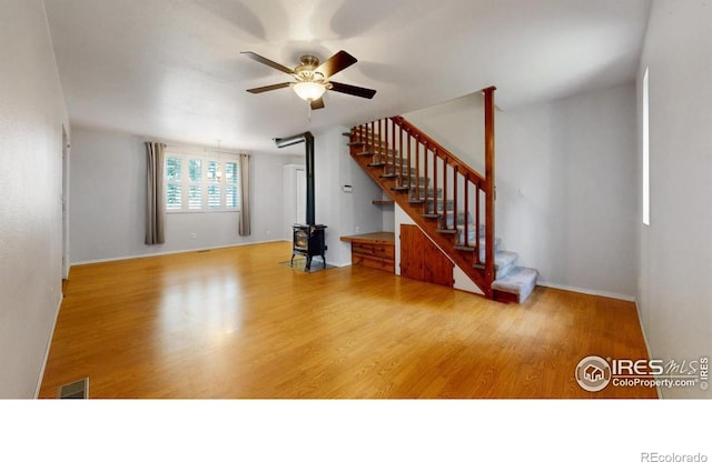 5001 W County Road 38 E, Fort Collins, CO 80526 - unfurnished living room featuring a wood stove, ceiling fan, wood finished floors, and stairs