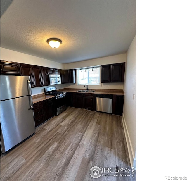 253 7th St, Frederick, CO 80530 - kitchen featuring stainless steel appliances, light wood finished floors, dark brown cabinets, and a textured ceiling