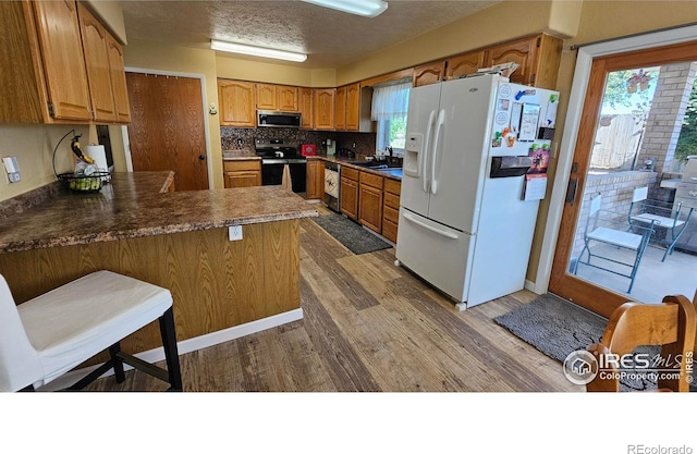 420 Applewood St, Brush, CO 80723 - kitchen with stainless steel appliances, wood finished floors, a peninsula, tasteful backsplash, and brown cabinets