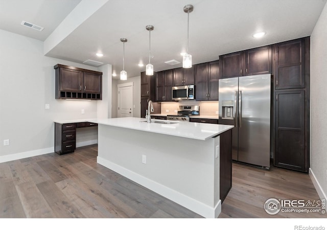 kitchen with appliances with stainless steel finishes, sink, dark brown cabinets, light hardwood / wood-style flooring, and a kitchen island with sink