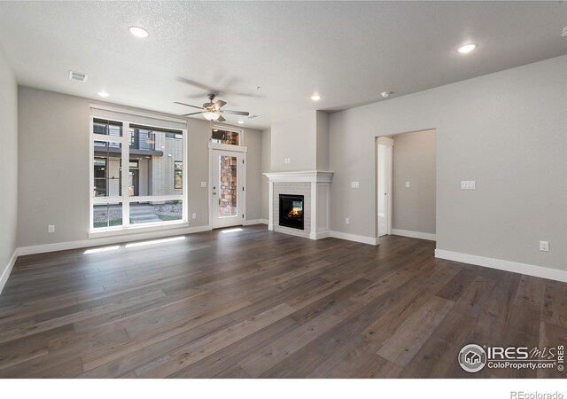 unfurnished living room with ceiling fan, a textured ceiling, and dark hardwood / wood-style flooring