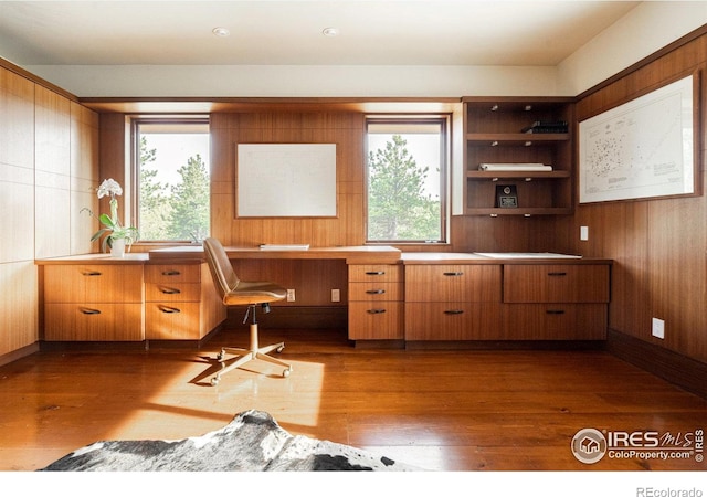 office featuring hardwood / wood-style flooring, wooden walls, and built in desk