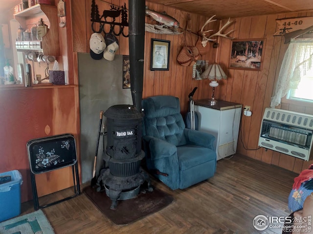 living area with heating unit, dark wood-type flooring, wooden walls, wooden ceiling, and a wood stove